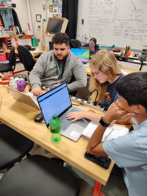 A mentor and two students working through equations at a laptop