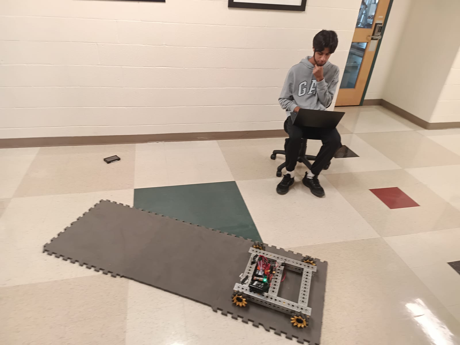 A student with a laptop watching the robot drive on tiles in the hallway