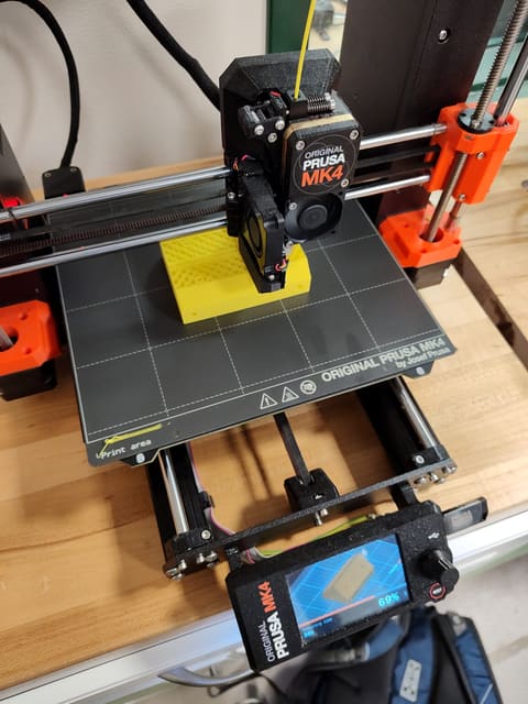 A 3D printer printing a yellow bracket