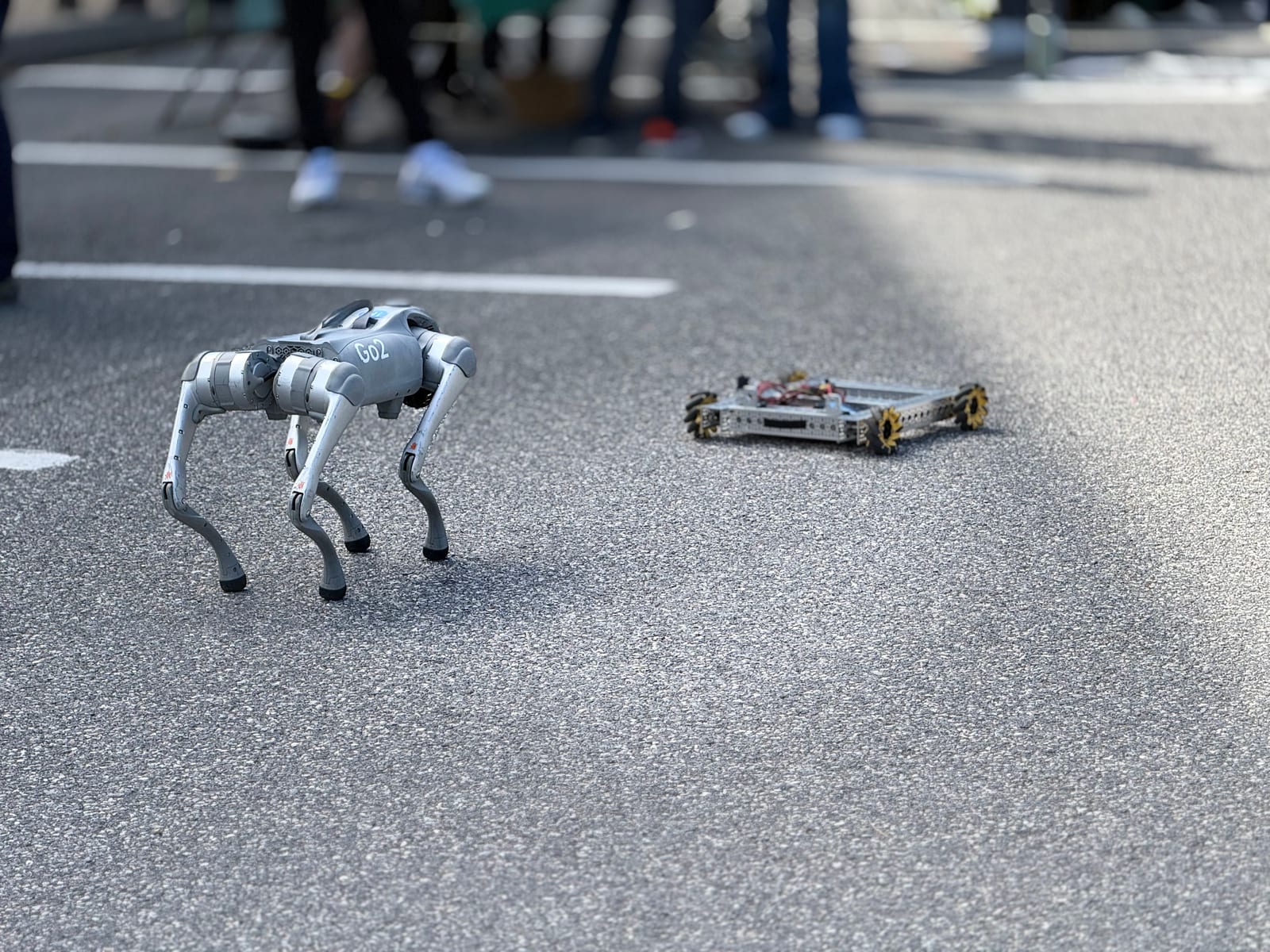 A Go2 robot dog beside our drive chassis on the pavement at Solar Science Day